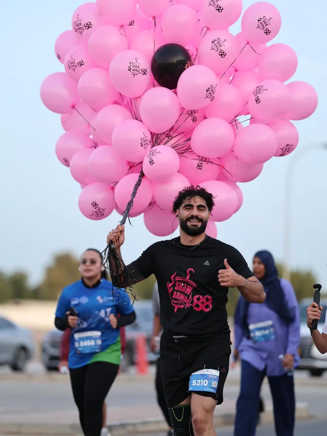 Shihab Mebarez running the Muscat Marathon 5 km with 100 helium balloons carrying the Shawarma 88 logo