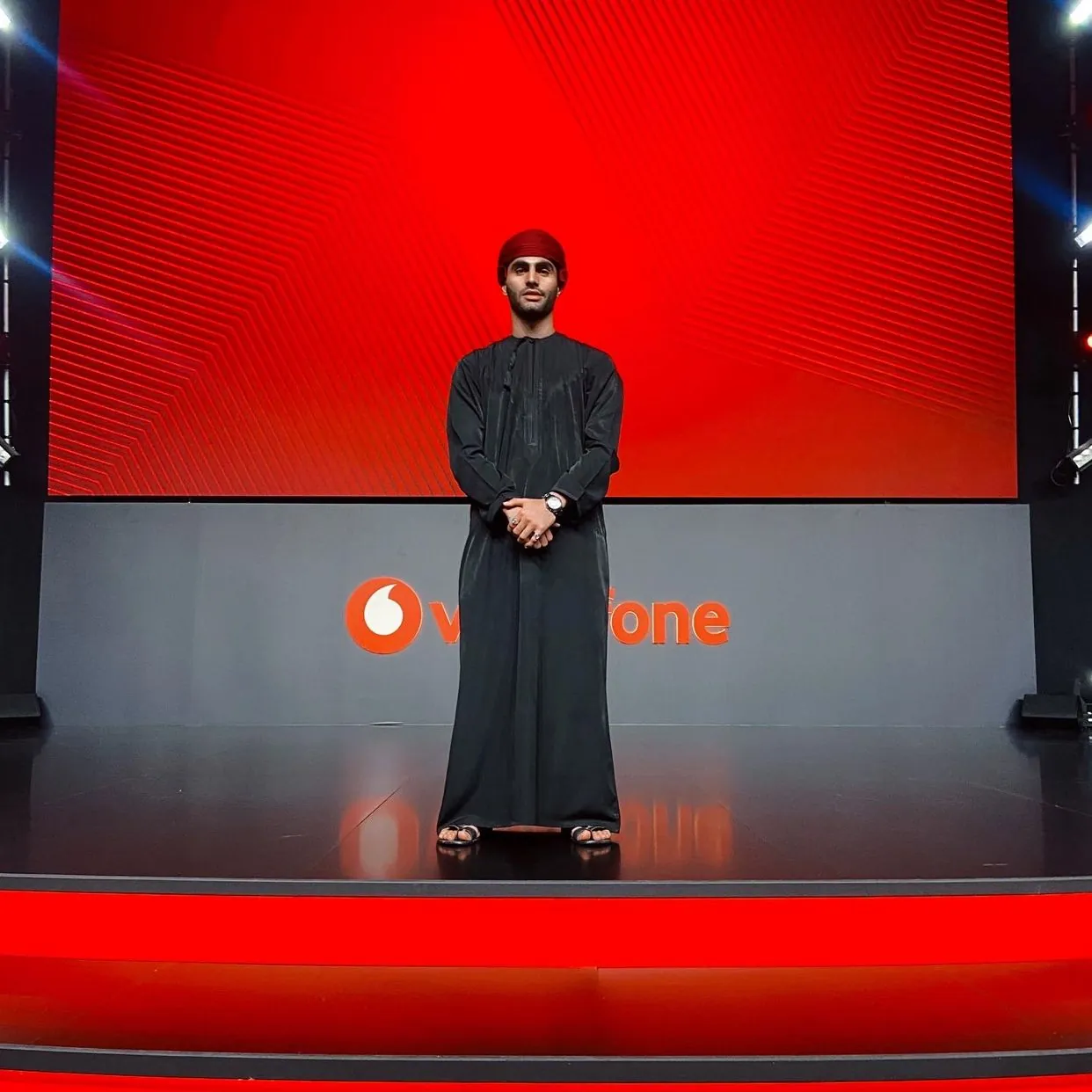 Shihab Mebarez on the stage of a Vodafone event, in a black dishdasha and red massar